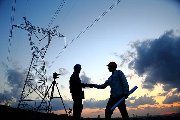 Silhouette of engineers standing at electricity station shaking hands.
